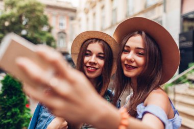 İki genç güzel moda kadın telefonu kullanarak selfie alarak açık portresi. Mutlu kız şehirde eğleniyor. Şapka giyen arkadaşlarım
