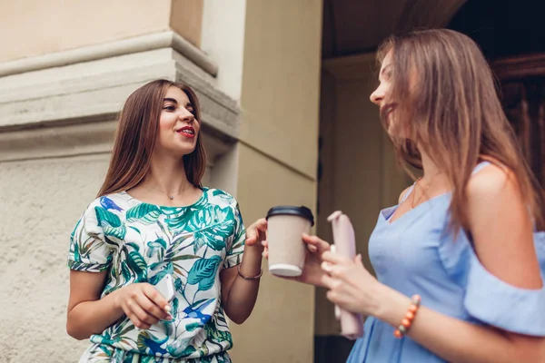 Two young beautiful women talking drinking coffee. Girls having fun in city. Best friends chat outdoors. College teens