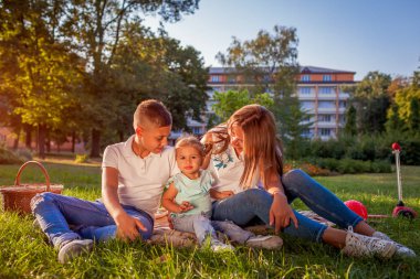 Mutlu bir aile zaman açık havada sittting Park çimenlerin üzerinde harcama. İki çocuk oğlu ve gülümseyen kızı annesiyle. Aile değerleri