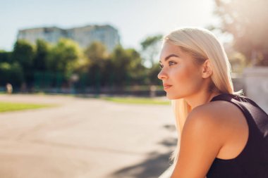 Genç kadın atlet sportsground üzerinde yaz aylarında çalıştırdıktan sonra dinlenme. Rahatlatıcı ve düşünme egzersiz yaptıktan sonra bankta oturan kız