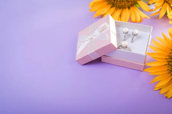 Set of pearl jewellery in the gift box with sunflowers on purple background