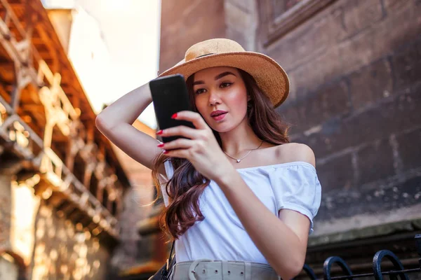 Young tourist woman searching for right way using navigator on smartphone. Stylish traveler girl walking on old city street