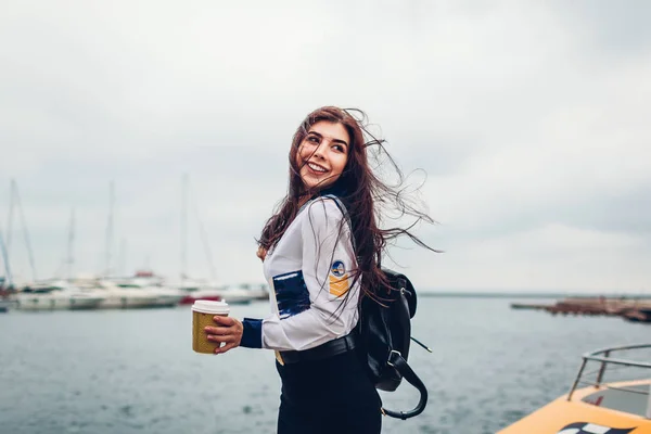 College woman student of Marine academy drinking coffee by sea wearing uniform. Girl walking in seaport of Odesa on pier