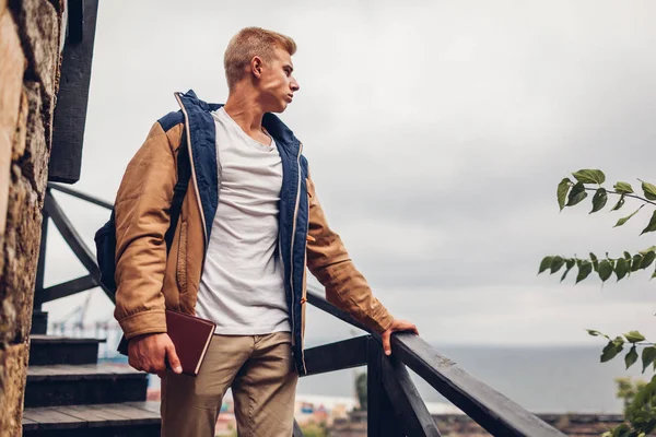 Sırt çantası ve deniz manzaralı Odessa'daki hayran kitap üniversite öğrencisi yağmurlu günde şehirde yürüyüş