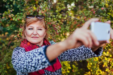 Selfie Park'ta yürüyordunuz telefon alarak orta yaşlı bir kadın. Üst düzey Bayan sonbahar ormanda eğleniyor