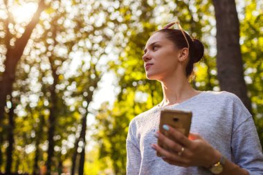 Parkta cep telefonuyla üniversite öğrencisi. Genç kadın holding smartphone açık havada.