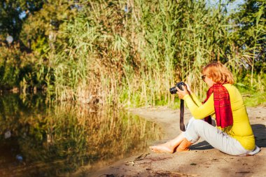 Orta yaşlı bir kadın görüntüleri camerasitting sonbahar nehir banka tarafından denetleniyor. Doğa ve fotoğraf çekim hobi zevk kadın kıdemli