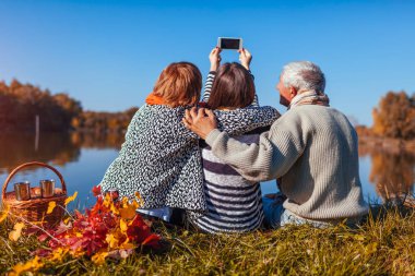 Yetişkin kızları ile sonbahar Gölü telefonla selfie alarak üst düzey anne. Aile değerleri. İnsanlar piknik