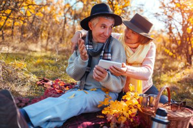 Üst düzey iki sonbahar ormanda çay yaparken telefon kullanarak. Mutlu bir adam ve konuşmak ve piknik ekranda gösteren kadın
