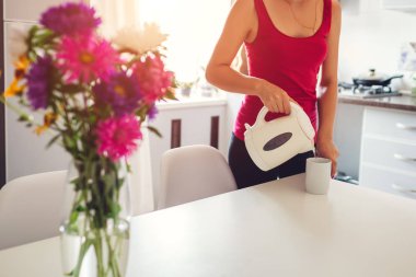 Kadın mutfakta elektrikli su ısıtıcısı sıcak su dökme. Çay yapmak kız. Modern mutfak tasarımı. Organik plastik kavramı