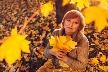 Akçaağaç buket tutan orta yaşlı kadın bırakır. Bayan sonbahar doğanın keyfini ve yere oturmuş rahatlatıcı