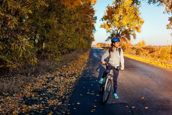 Young bicyclist riding in autumn field at sunset. Happy woman smiling. Active way of life