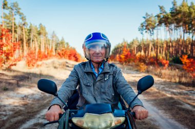 Komuta sizde binme scooter sonbahar orman yolu üzerinde. Motosiklet Binme kask içinde mutlu sürücü.