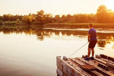 Genç gün batımında ayakta Nehri Köprüsü'nde balık adam. Yaz aylarında hobi zevk mutlu fiserman