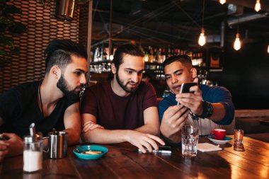 Grup konuşuyor ve telefon lounge barda kullanarak karma yarış genç adam. Çok ırklı arkadaşlar eğlenmeye kafede