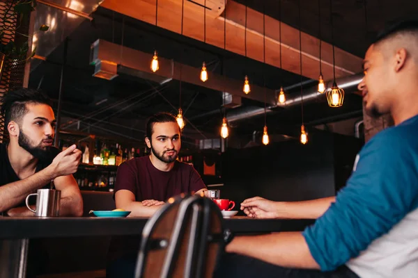 Group of mixed race young men talking and laughing in lounge bar. Multiracial friends having fun in cafe. Guys hang out