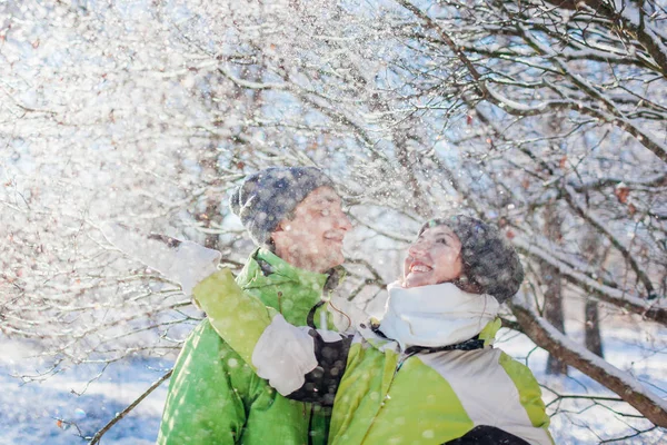 Couple in love throwing snow and hugging in winter forest. Young people having fun during holidays