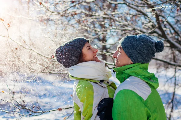 Couple in love throwing snow and hugging in winter forest. Young people having fun during holidays