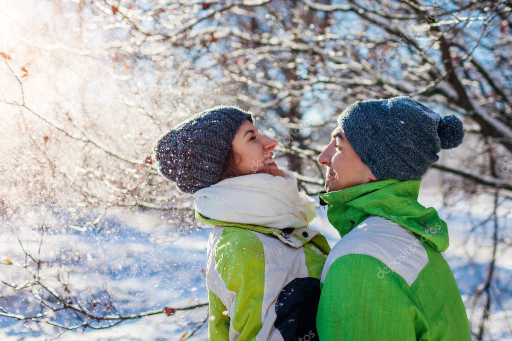 Couple in love throwing snow and hugging in winter forest. Young people having fun during holidays
