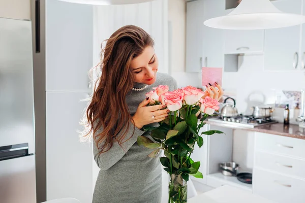 若い女性は 台所でカードとバラの花束を発見しました 幸せな興奮して女の子の花の臭いがします バレンタインの日 — ストック写真