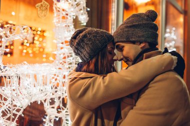 Genç çift tatil kafeye sarılma sevgi dolu ile dekore edilmiş reindeers geceleri vitrin. Noel ve yeni yıl kavramı