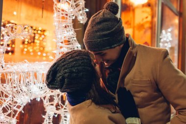 Genç çift tatil kafeye sarılma sevgi dolu ile dekore edilmiş reindeers geceleri vitrin. Noel ve yeni yıl kavramı