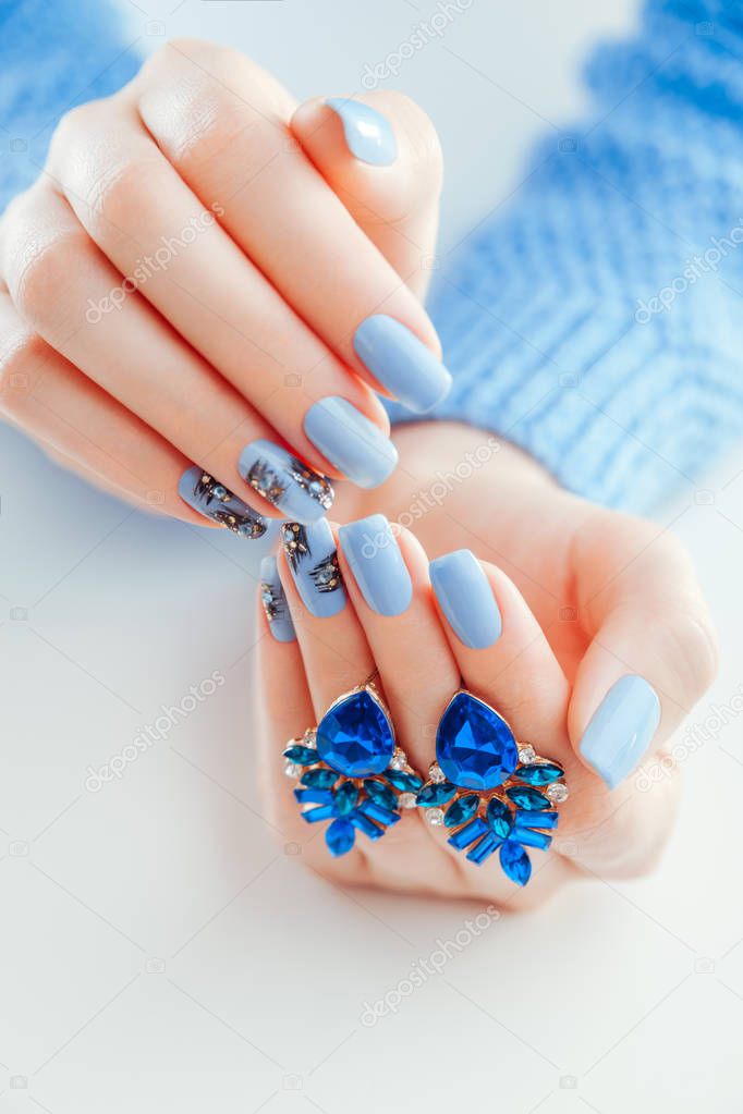 Beautiful Christmas manicure with earrings. Blue nails with black design, rhinestones and jewellery. Body care concept