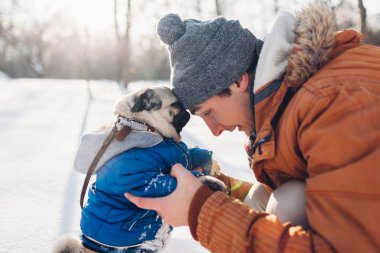 Efendisinin ile karda yürüyen pug köpek. Köpek yavrusu giyen kışlık mont. Adam kış ormanda hayvanını sarılma. Hayvanlar için giyim