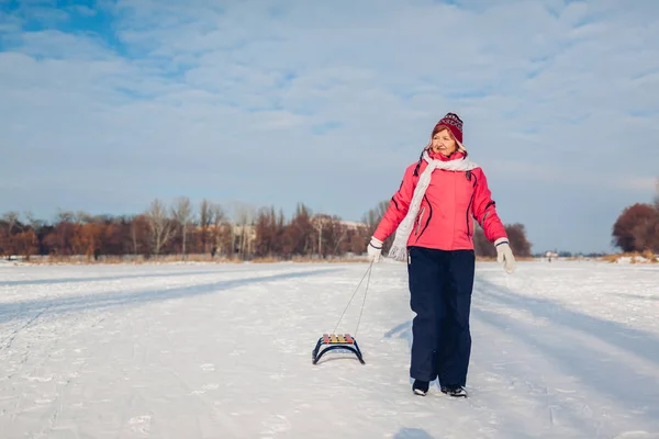上了年纪的女人滑倒后带着雪橇 在冬日冰冻的河里玩得开心的女人 积极的生活方式 — 图库照片