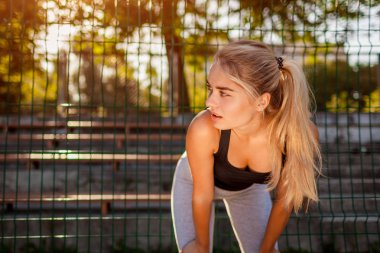 Genç kadın atlet sportsground üzerinde yaz aylarında çalıştırdıktan sonra dinlenme. Açık havada sabah rahatlatıcı ve tüyler ürpertici kız