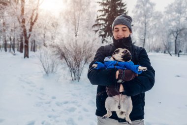 Efendisinin ile karda yürüyen pug köpek. Köpek yavrusu giyen kışlık mont. Hayvanını kış orman içinde tutan adam. Hayvanlar için giyim