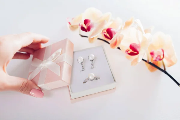 Woman opens a gift box with a set of perl jewellery with yellow orchid. Present for Valentine\'s day with flowers