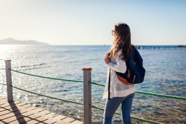 Genç kadın turist Kızıldeniz ve Tiran Adası iskelede yürüyüş manzara hayran sırt çantası ile. Kavram seyahat. Yaz tatili