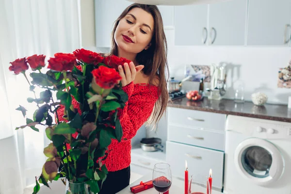 年轻女子在厨房里发现了一束玫瑰花 上面有蜡烛 葡萄酒和礼品盒 快乐的女孩闻到鲜花的味道 情人节惊喜 — 图库照片