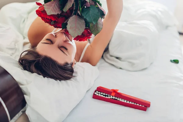 若い女性は ベッドでギフト ボックスのジュエリーとバラの花束を発見しました 幸せな女の子の花の臭いがします 女性の日サプライズ — ストック写真