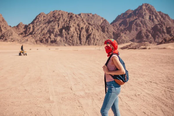 Tourist woman with backpack wearing scarf on head. Traveler admiring Sinai Desert and mountains. Summer vacation