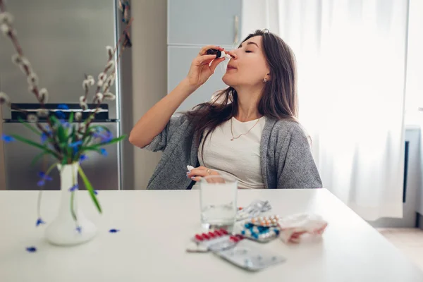 Lente allergie. Vrouw met behulp van nasale druppels tegen seizoensgebonden allergie en nemen pillen op keuken. Gezondheidszorg en geneeskunde — Stockfoto