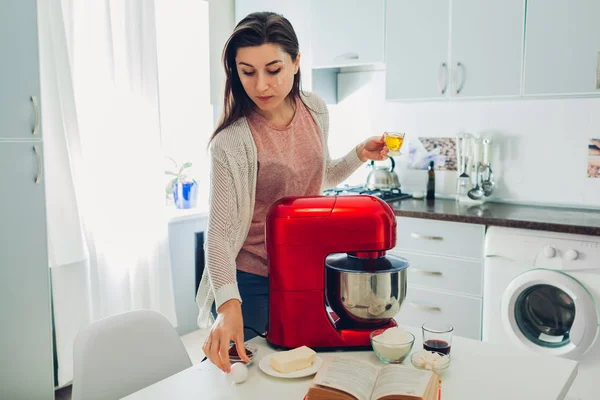 Pastel de cocina de ama de casa joven según la receta en el libro culinario. Mujer usando procesador de alimentos en la cocina — Foto de Stock