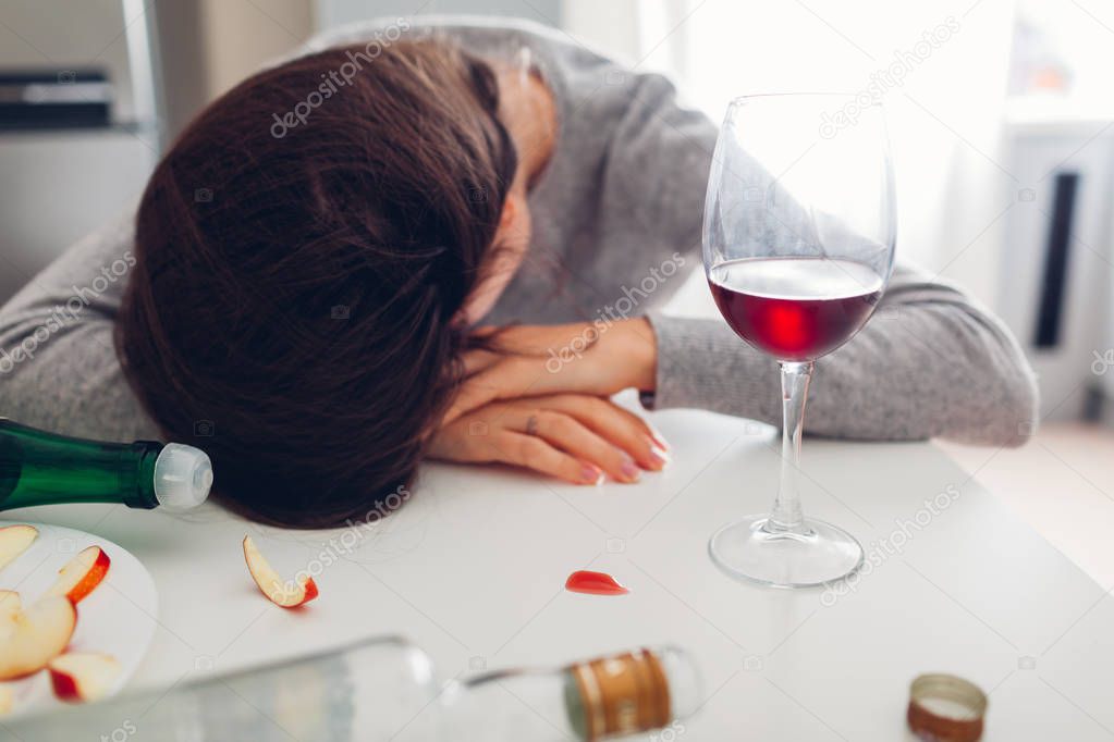 Female alcohol addiction. Young woman sleeping on kitchen table surrounded with wine bottles