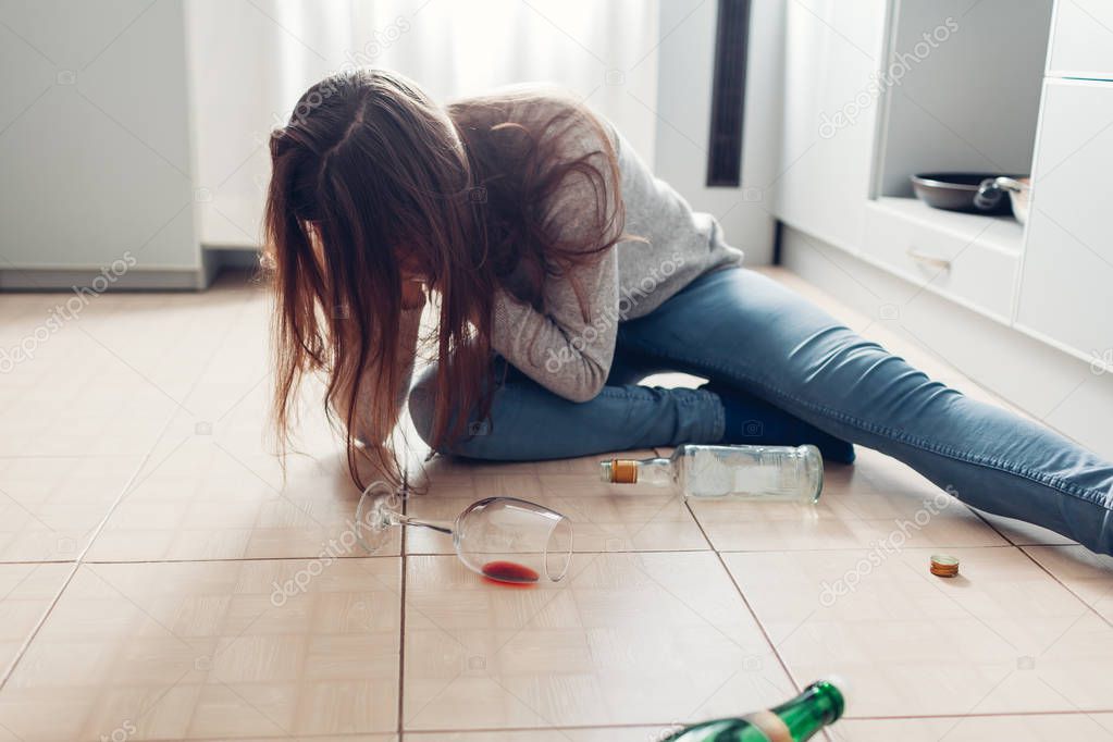 Female alcohol addiction. Young woman woke up on kitchen floor after party surrounded with wine bottles. Hangover