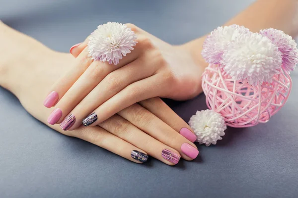 Ροζ και μαύρο μανικιούρ σε γυναικεία χέρια με λουλούδια σε γκρίζο φόντο. Τέχνη νυχιών και σχεδιασμός — Φωτογραφία Αρχείου