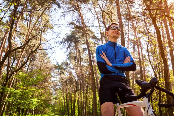 Young man bicyclist riding a road bike in spring forest. Man having rest