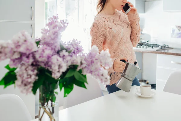 Женщина наливает кофе из чайника на кухню, разговаривая по телефону. Завтрак — стоковое фото