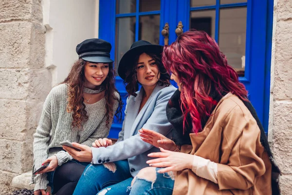 На улице снимали трех молодых женщин, смотрящих на смартфон на улице. Девушки разговаривают и веселятся — стоковое фото