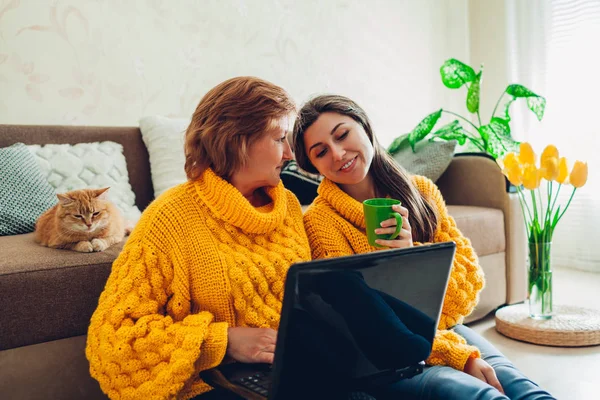 Senior anya és felnőtt lánya segítségével laptop otthon, miközben teát iszik. Anyák napi koncepció. — Stock Fotó