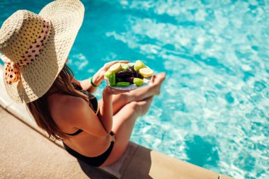 Kadın meyve yeme ve yüzme havuzunda rahatlatıcı bikini. Herşey dahil. Yaz tatili