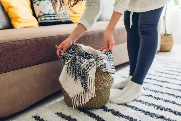 Young woman puts blanket in straw basket. Interior decor of living room