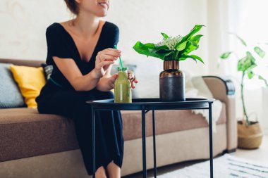 Oturma odasında dinlenen ve smoothie içen genç bir kadın. Ev konforu ve konfor
