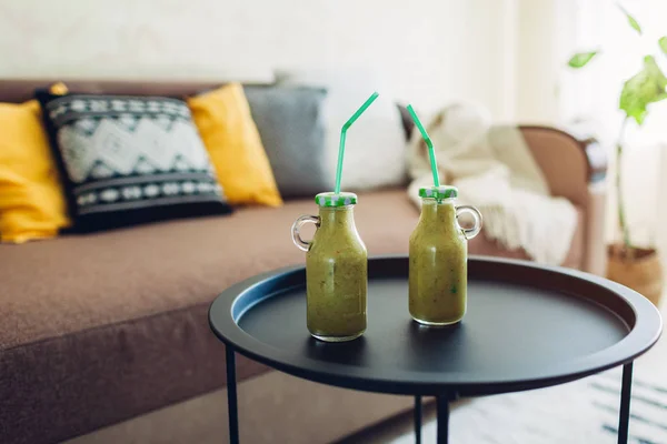 Dos botellas de batido frutal verde en la mesa de la sala de estar. Beber bebidas desintoxicantes saludables en casa — Foto de Stock