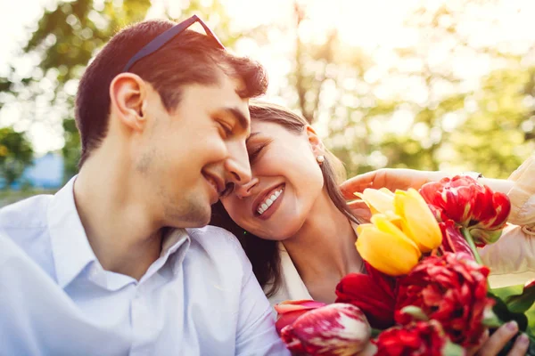 Joyeux jeune couple amoureux étreignant avec bouquet de fleurs de printemps à l'extérieur. Homme doué sa petite amie avec des tulipes — Photo